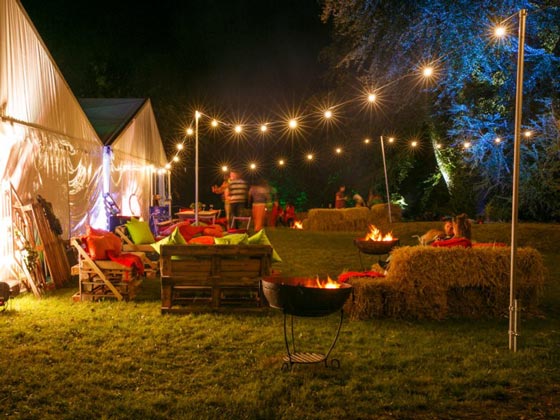 Festoon Lighting Supported by 3 Meter High Scaffold Poles, with Burning Kadai Fire Pits at Night Time