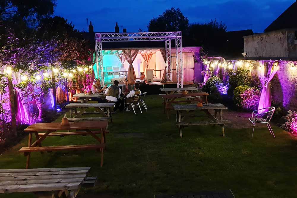 A back garden has been transformed with festoon lighting and colourful rgb LED uplighters to create an outdoor music event.