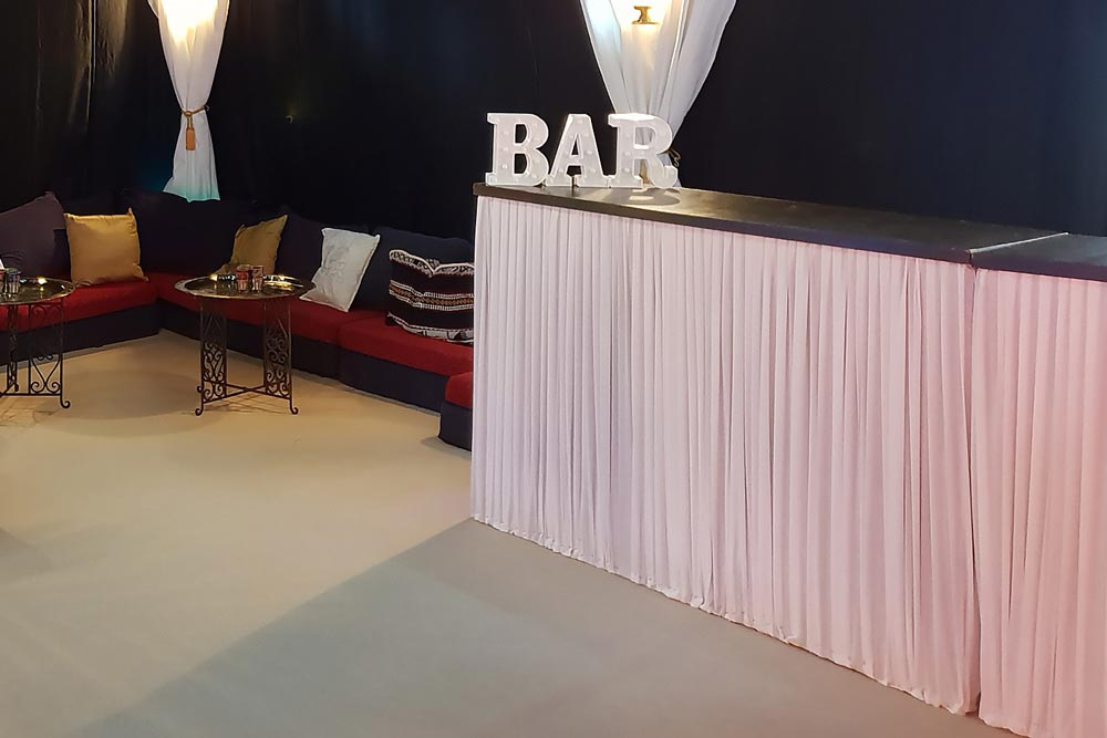 An elegant wooden bar unit with a custom white pleated cotton cover