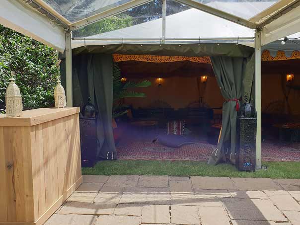 A clear roof walkway marquee contecting to Bedouin tents and containing a rustic champagne bar.